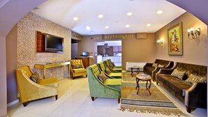 Vestíbulo de hotel con mostrador de recepción, televisión y letrero de restaurante.