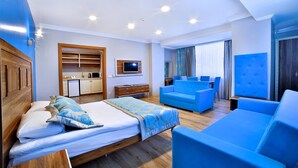 Una habitación de hotel moderna con una cama grande, un sofá azul, una televisión y una kitchenette.