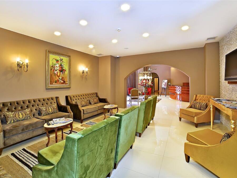 Eine großzügige Lobby mit einer Couch, Sesseln und einem Couchtisch. Eine Rezeption sowie ein an der Wand befestigter Fernseher sind vorhanden.
