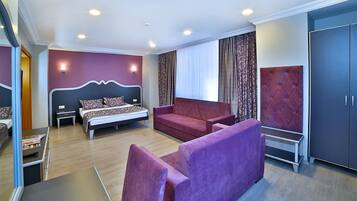 A modern hotel room with a bed, a sofa, a desk, and a wardrobe.