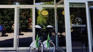 En hotelindgang med en glasdør, to cykler med cykelhjelme, og et skilt til hotellet.
