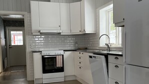 A modern kitchen with white cabinets, a built-in oven, a refrigerator, and a window providing natural light. - Helsingegården (Jarvso)