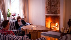 A cozy living room with a fireplace, striped sofas, and a round wooden table. - Helsingegården (Jarvso)