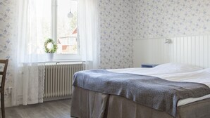 A bedroom with a bed, a radiator, a window with curtains, and a potted plant. - Helsingegården (Jarvso)