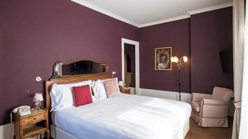 Quarto com cama grande, mesa de cabeceira com abajur, cadeira e um quadro na parede.