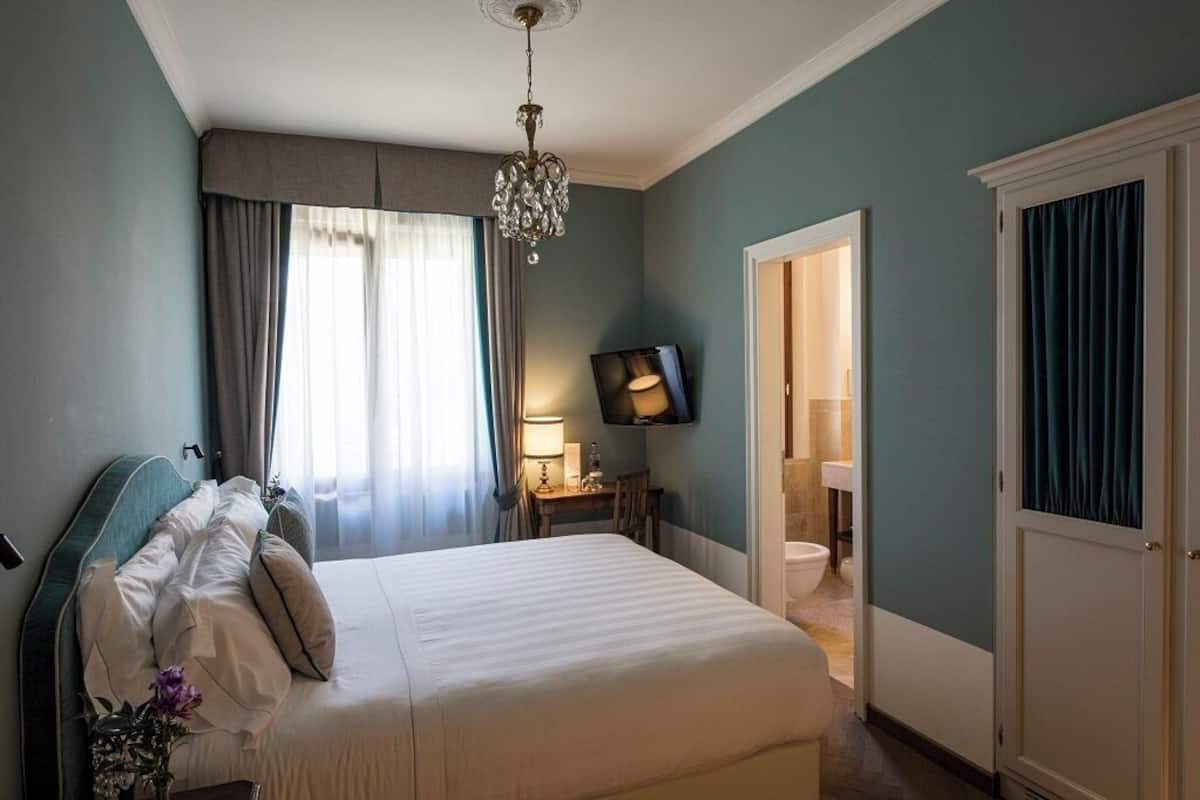 A hotel room with a bed, a television, a desk with a lamp, and a bathroom visible through an open door.