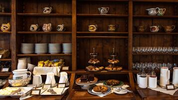 Um buffet de café da manhã com diversos alimentos, utensílios e cerâmica decorativa em prateleiras.