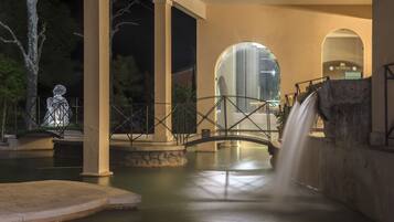 Ein Nachtbild einer Brücke über einem Wasserspiel mit einem Wasserfall, umgeben von Säulen und Bögen aus Stein.