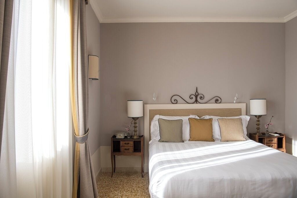 A hotel room with a large bed, two bedside tables with lamps, and a window with curtains.