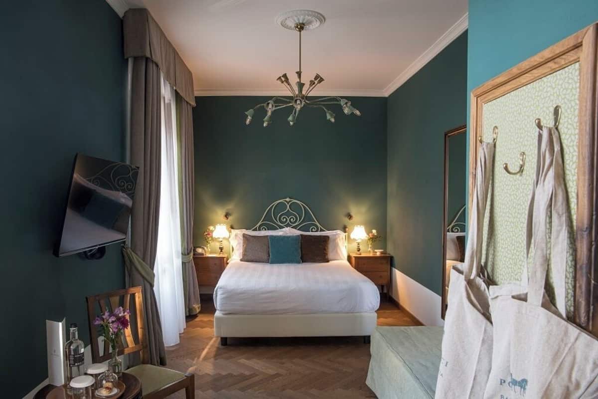 A neatly arranged bedroom with a bed, bedside tables, a TV mounted on the wall, and a chandelier.