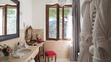 A bathroom with two sinks, a mirror, a chandelier, a window with curtains, and a red stool.