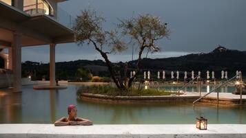 A pool area with a person relaxing, a tree, and a lantern.