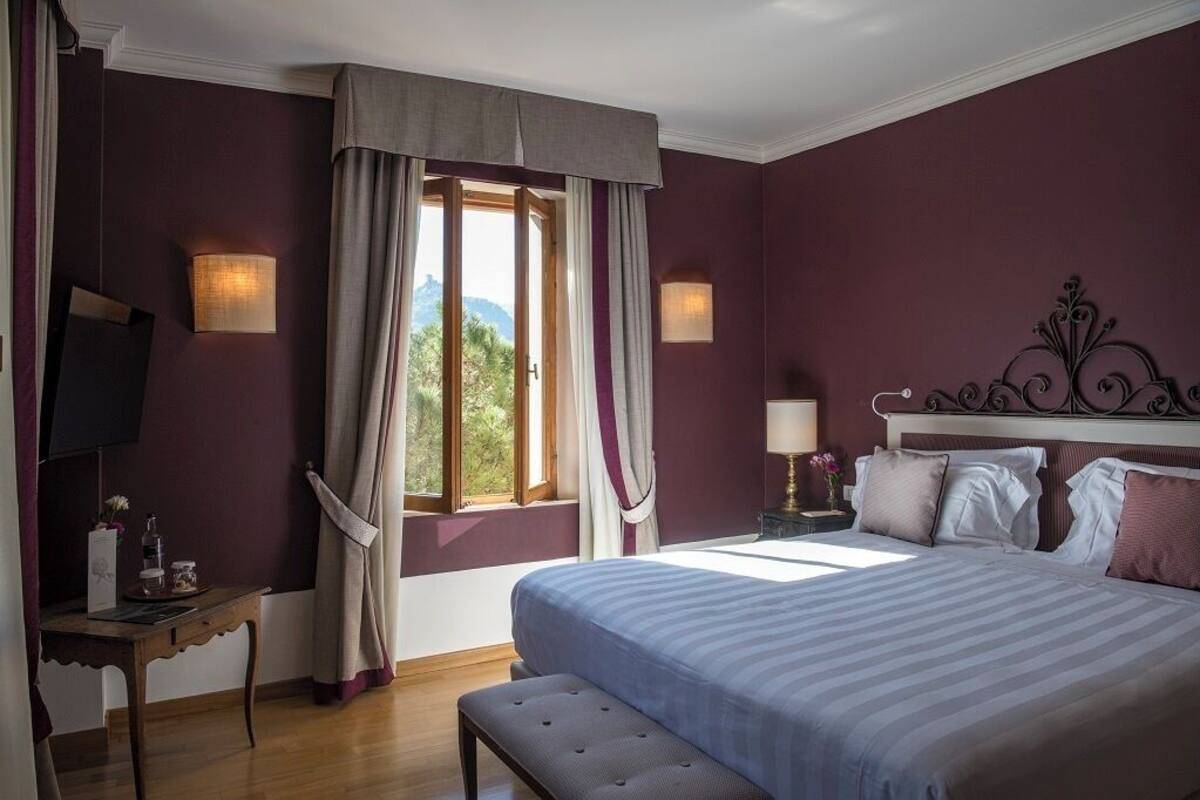 A bedroom with a large bed, a bedside table, a TV, and a window with curtains.