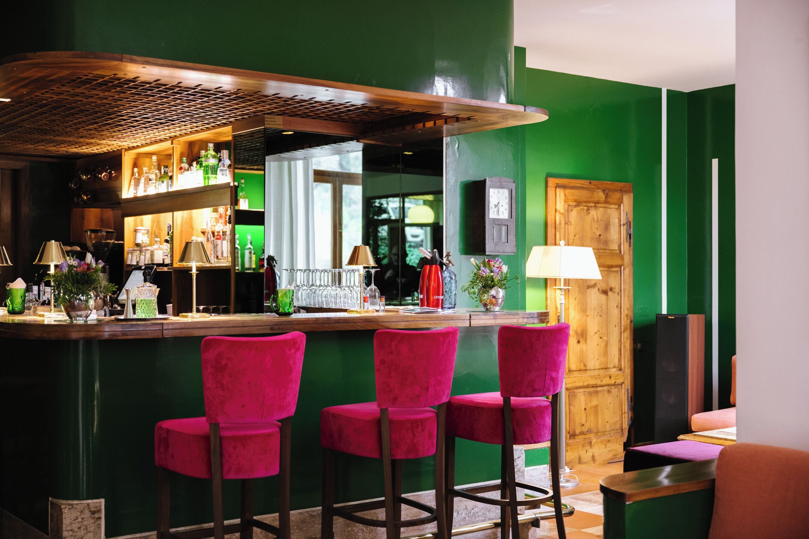 Un espace bar avec des murs verts, un comptoir en bois et trois tabourets de bar roses.