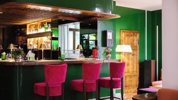 Un espace bar avec des murs verts, un comptoir en bois et trois tabourets de bar roses.