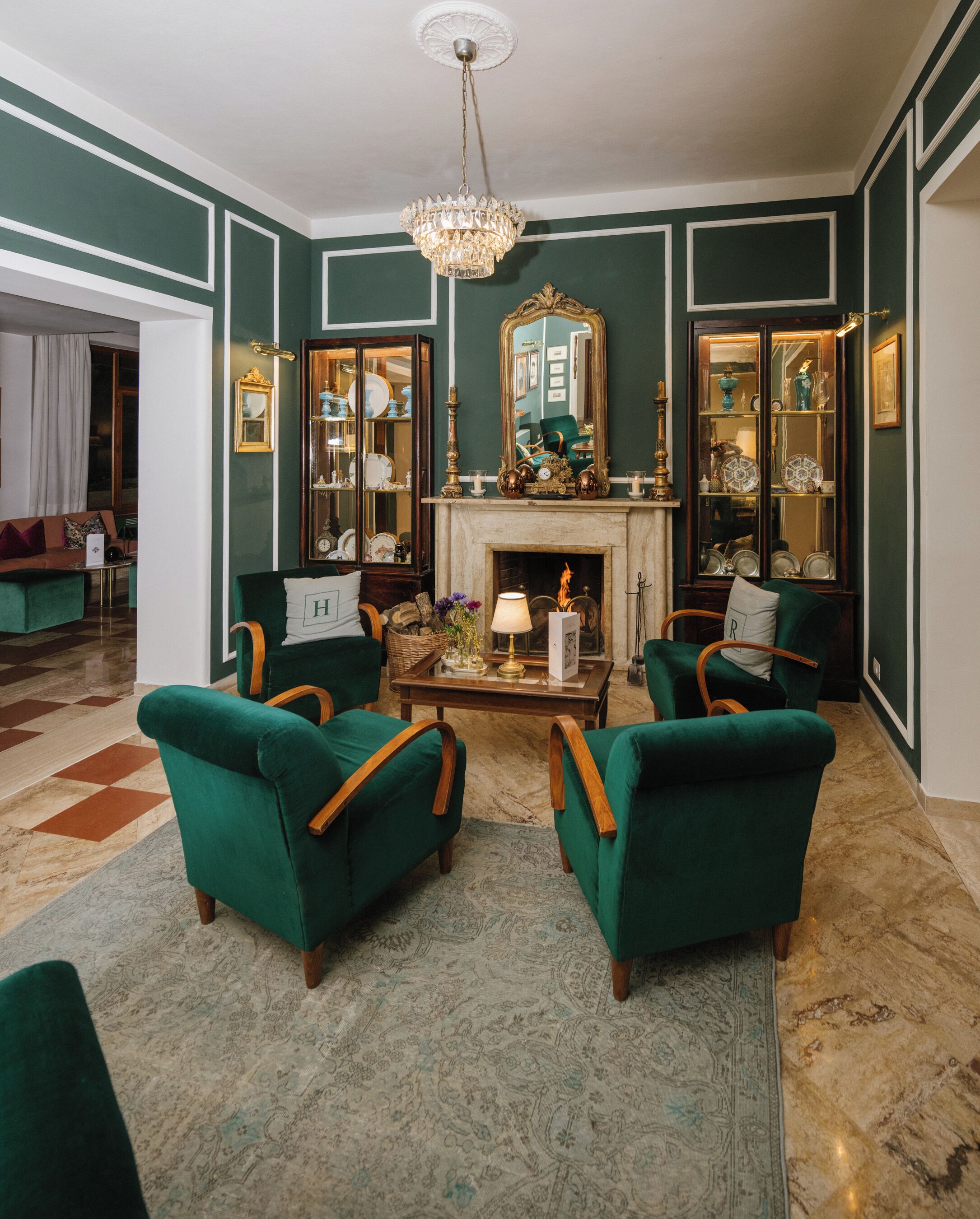 Una habitación con sillones tapizados en verde, una mesa de centro de madera, una chimenea y un espejo grande.