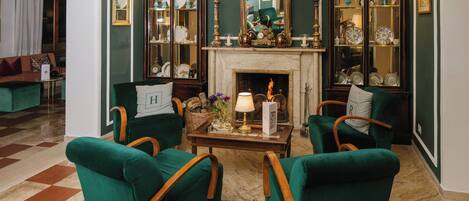 Una habitación con sillones tapizados en verde, una mesa de centro de madera, una chimenea y un espejo grande.