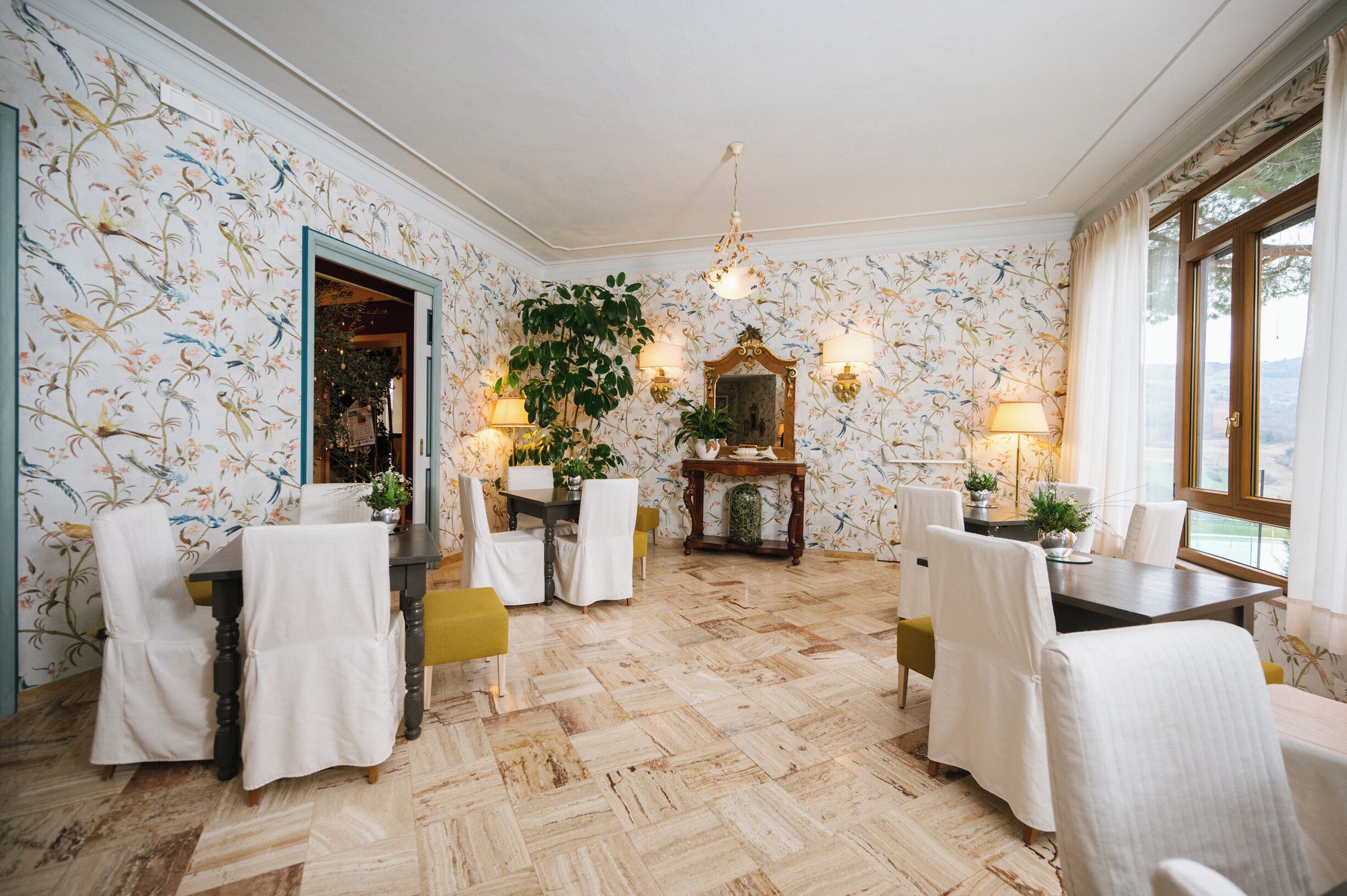 A dining area with a herringbone floor, floral wallpaper, and a large mirror above the table.