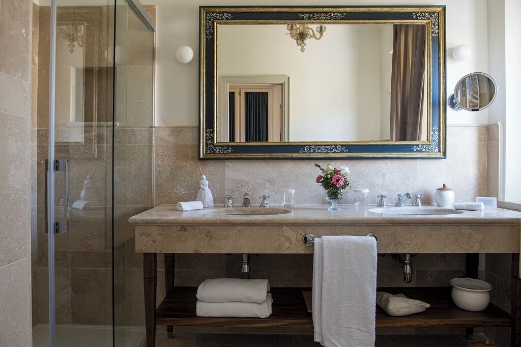 A bathroom with a large mirror, two sinks, a shower, and a vanity with a towel rack.