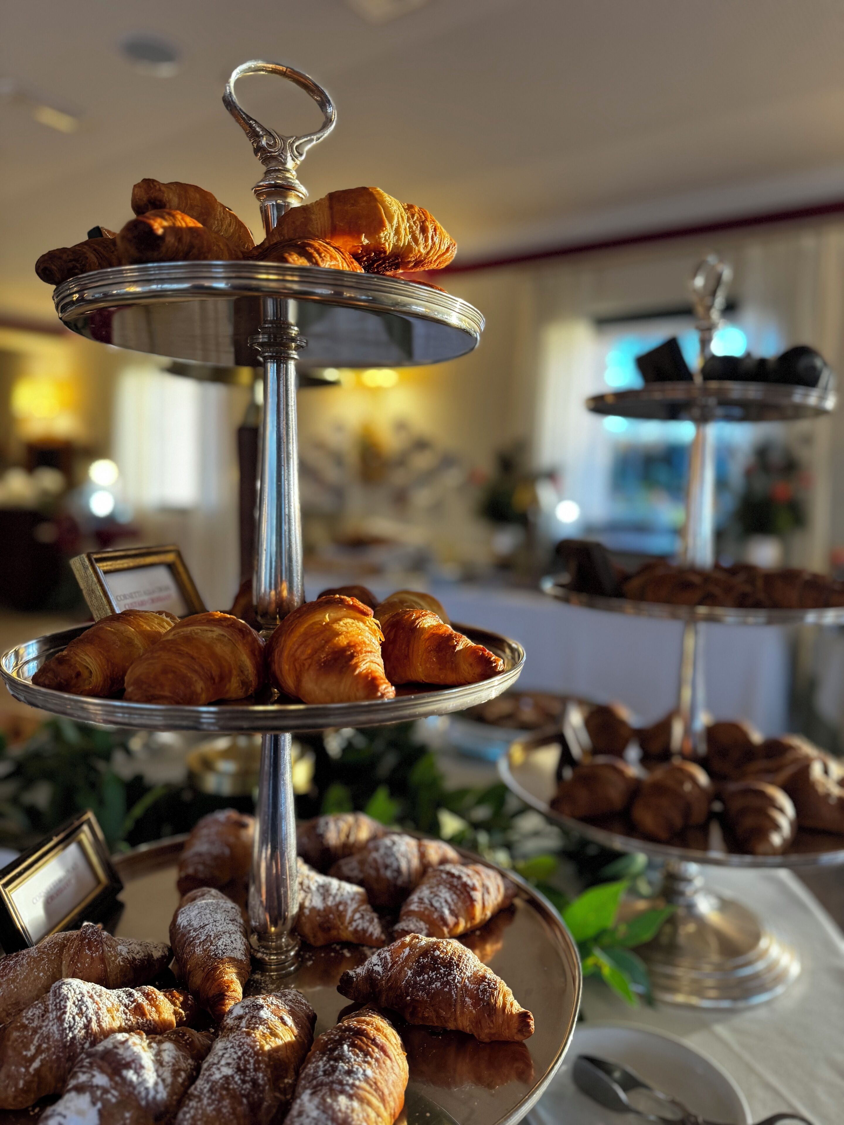 A multi-tiered display of pastries, including croissants and other baked goods, arranged on a metal stand.