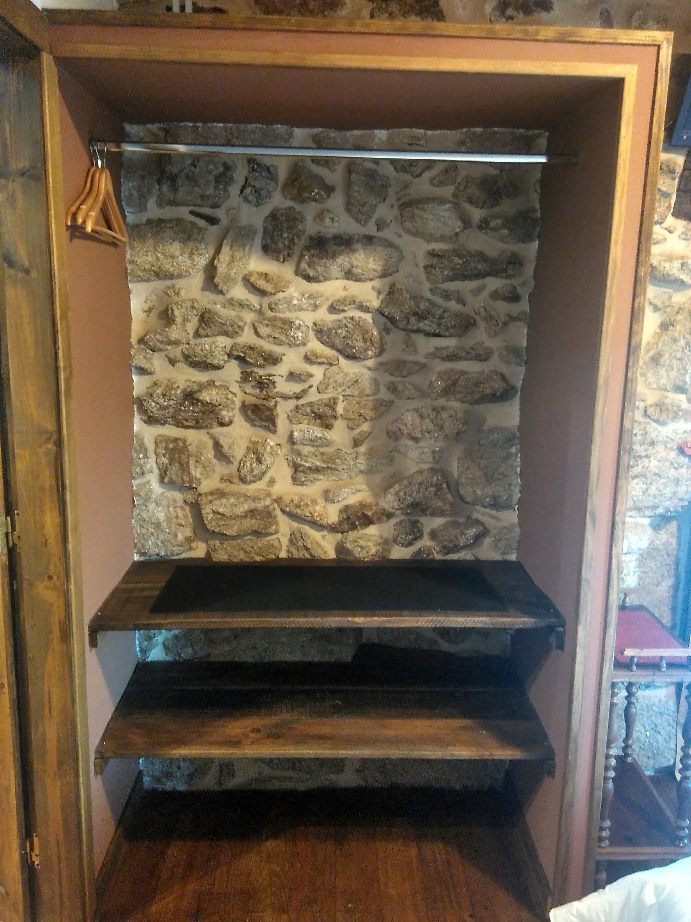 Un muro de piedra con un estante de madera y un marco de puerta de madera.