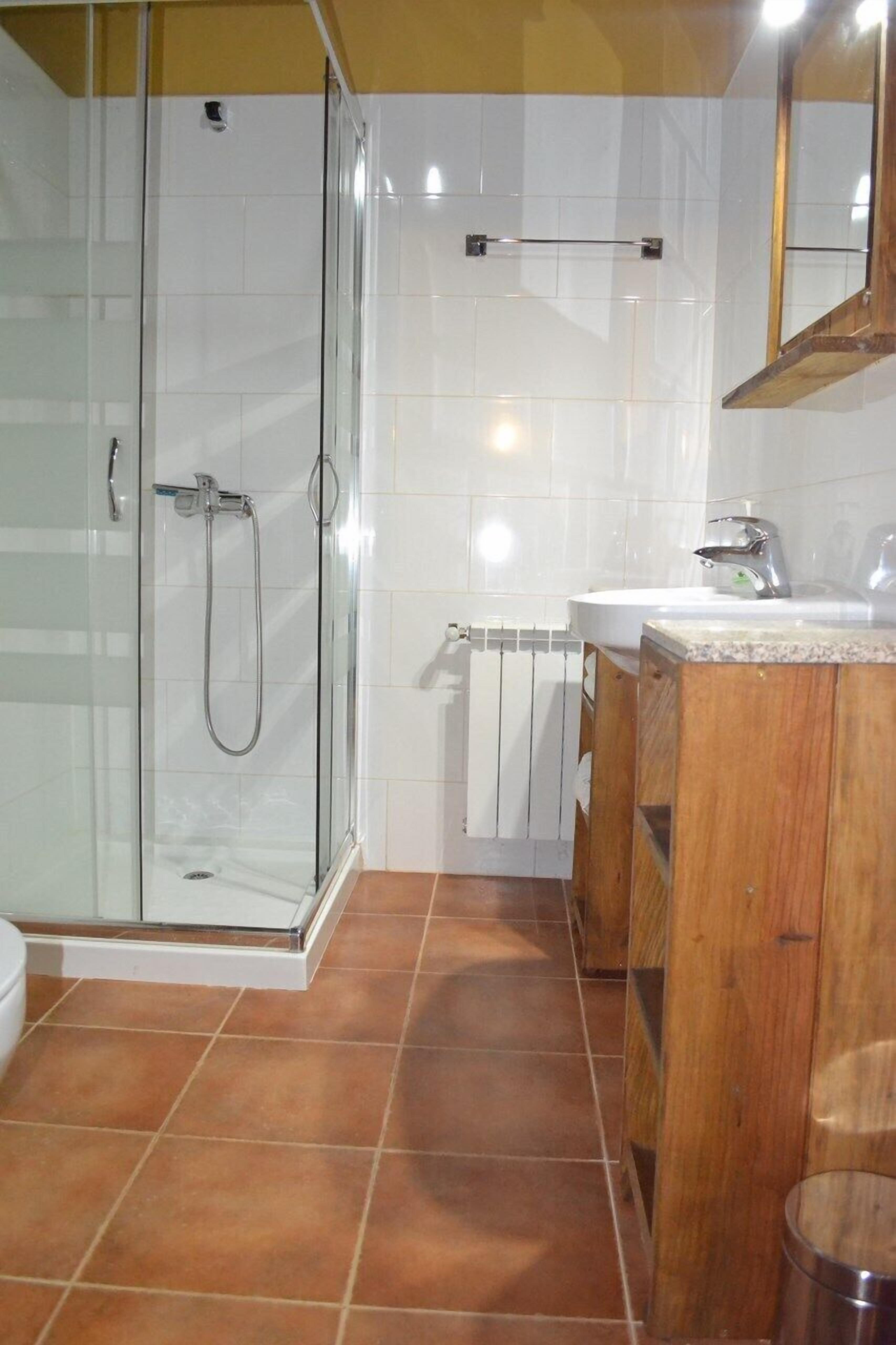 Un baño con cabina de ducha de vidrio, tocador de madera y lavamanos blanco.