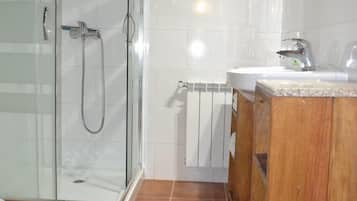 Un baño con cabina de ducha de vidrio, tocador de madera y lavamanos blanco.