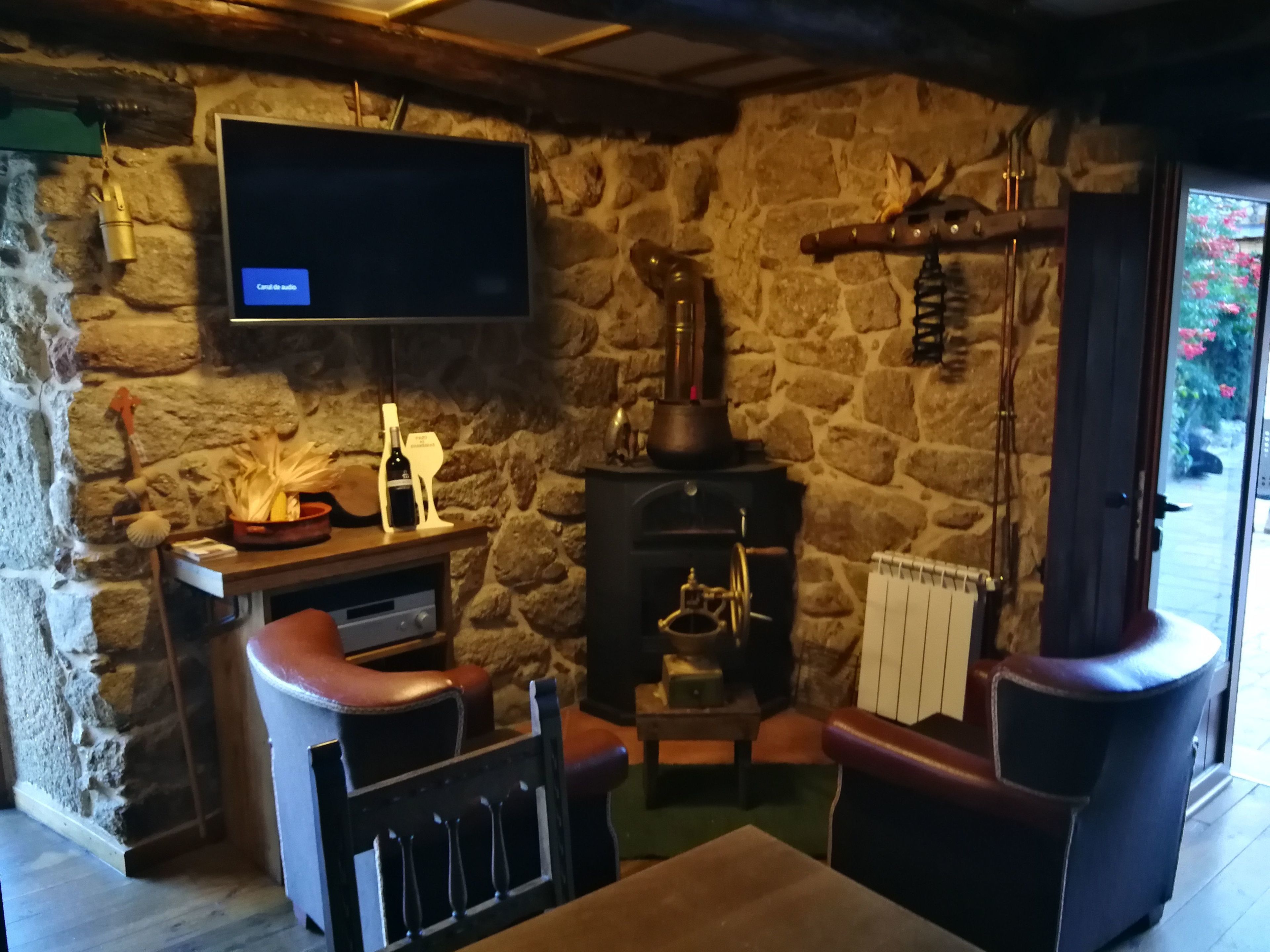 Una habitación rústica con pared de piedra, chimenea, televisor montado en la pared y sillones de cuero.