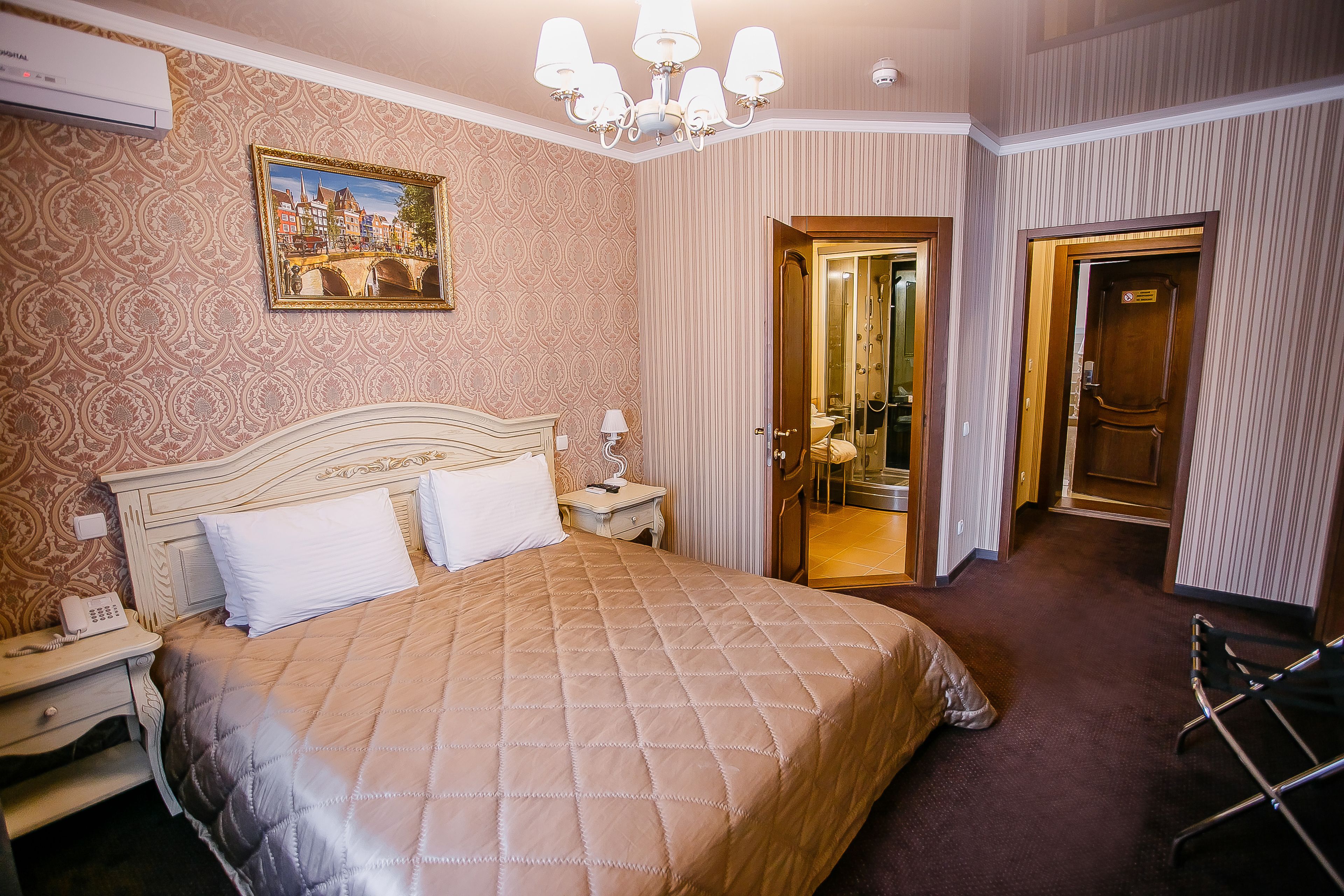 Ein Hotelzimmer mit einem großen Bett, einem Nachttischtelefon, einem Spiegel und einer Tür zu einem Badezimmer.