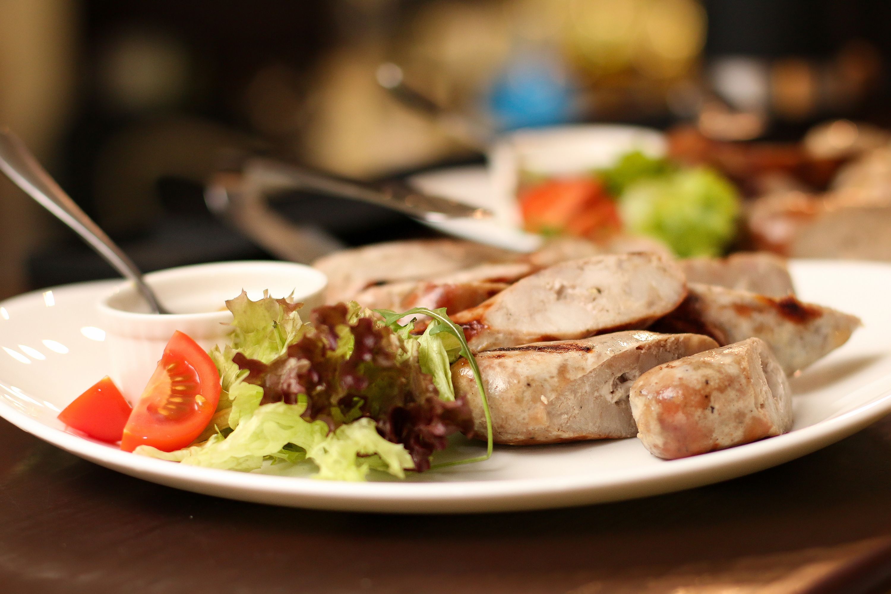 A plate with grilled sausages, a slice of tomato, and a small salad on a white plate.