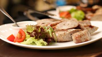 A plate with grilled sausages, a slice of tomato, and a small salad on a white plate.