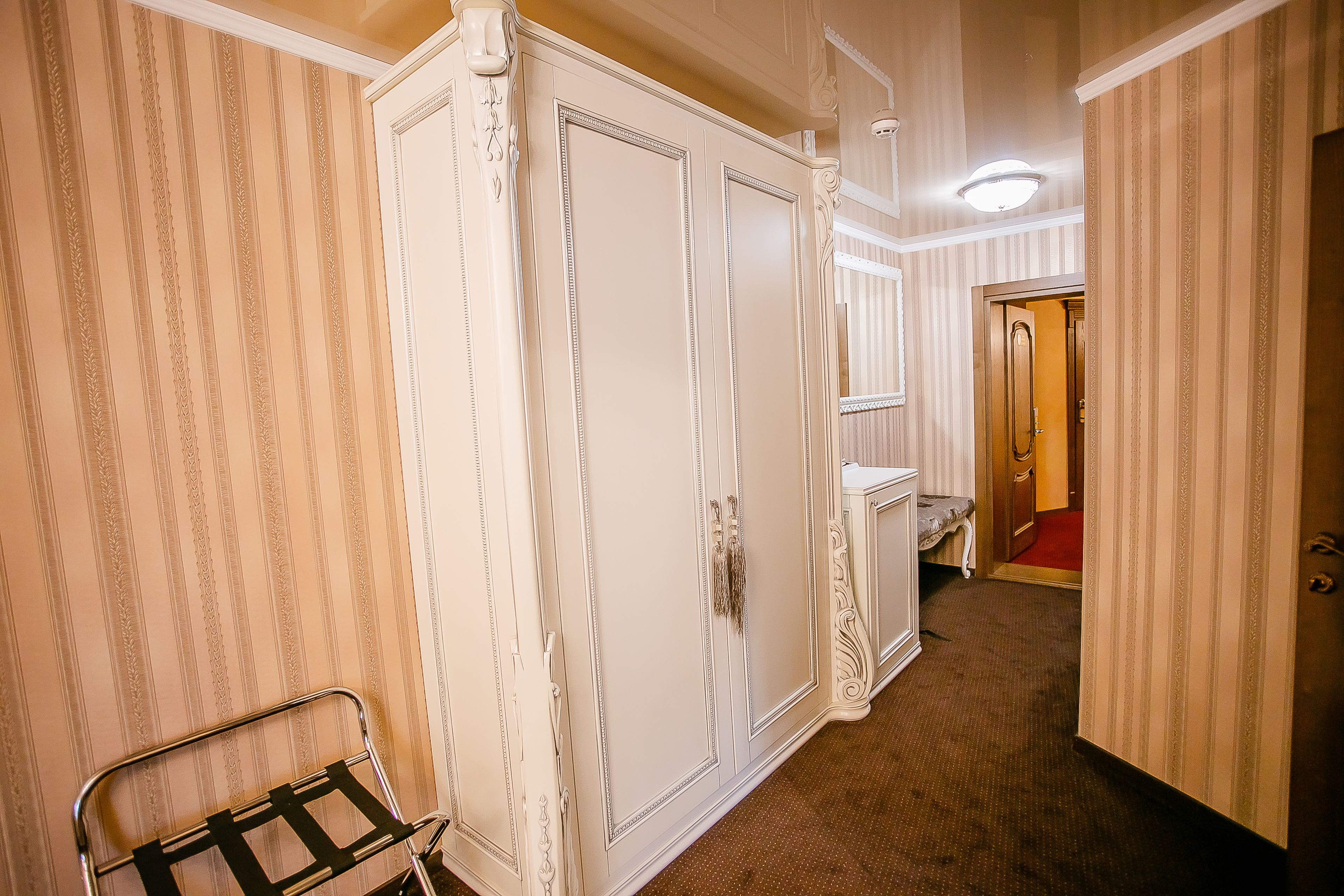 A hallway with striped wallpaper, a white wardrobe with decorative trim, and a metal chair.