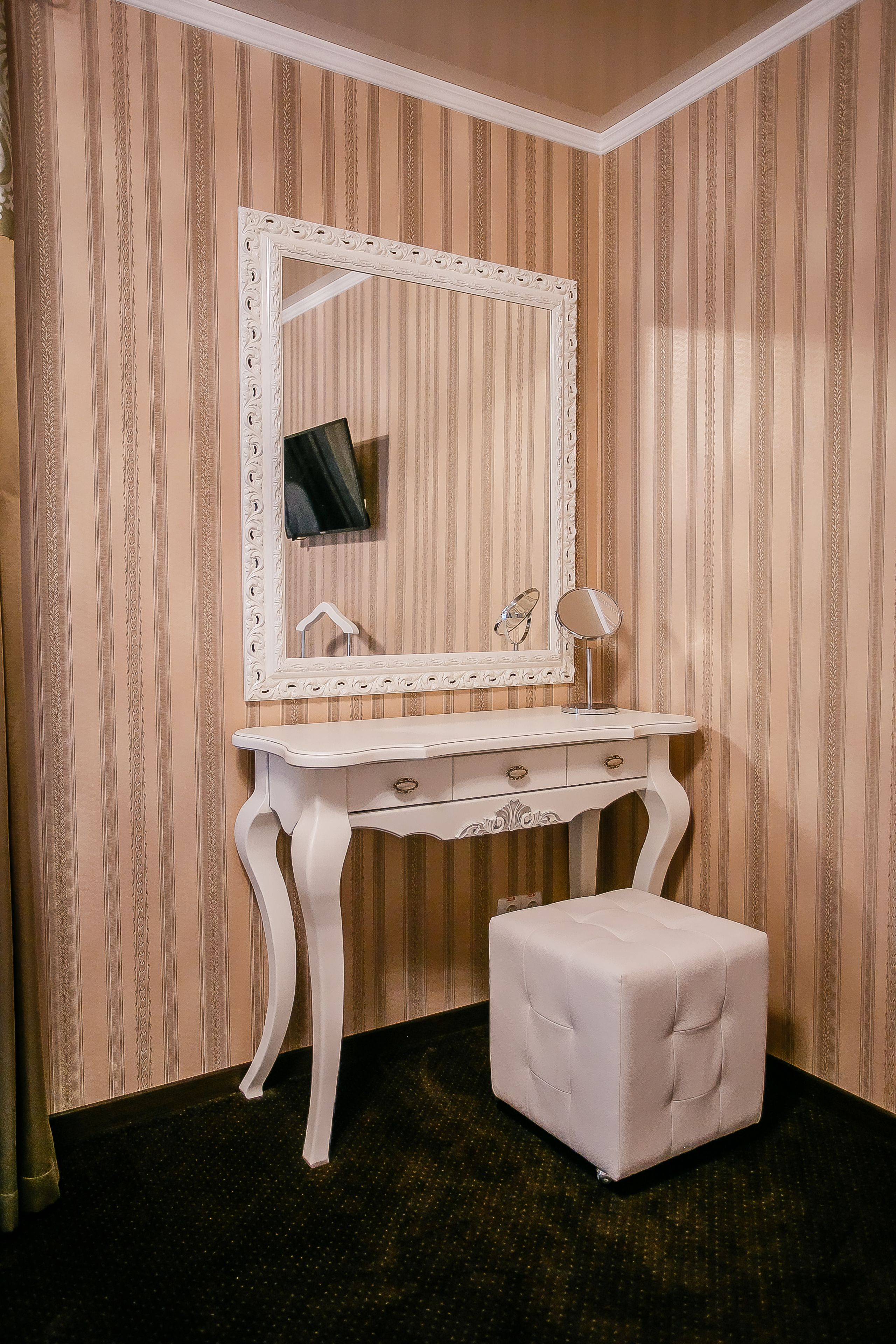 A vanity with a large mirror, a small table, and a stool in a room with striped wallpaper.