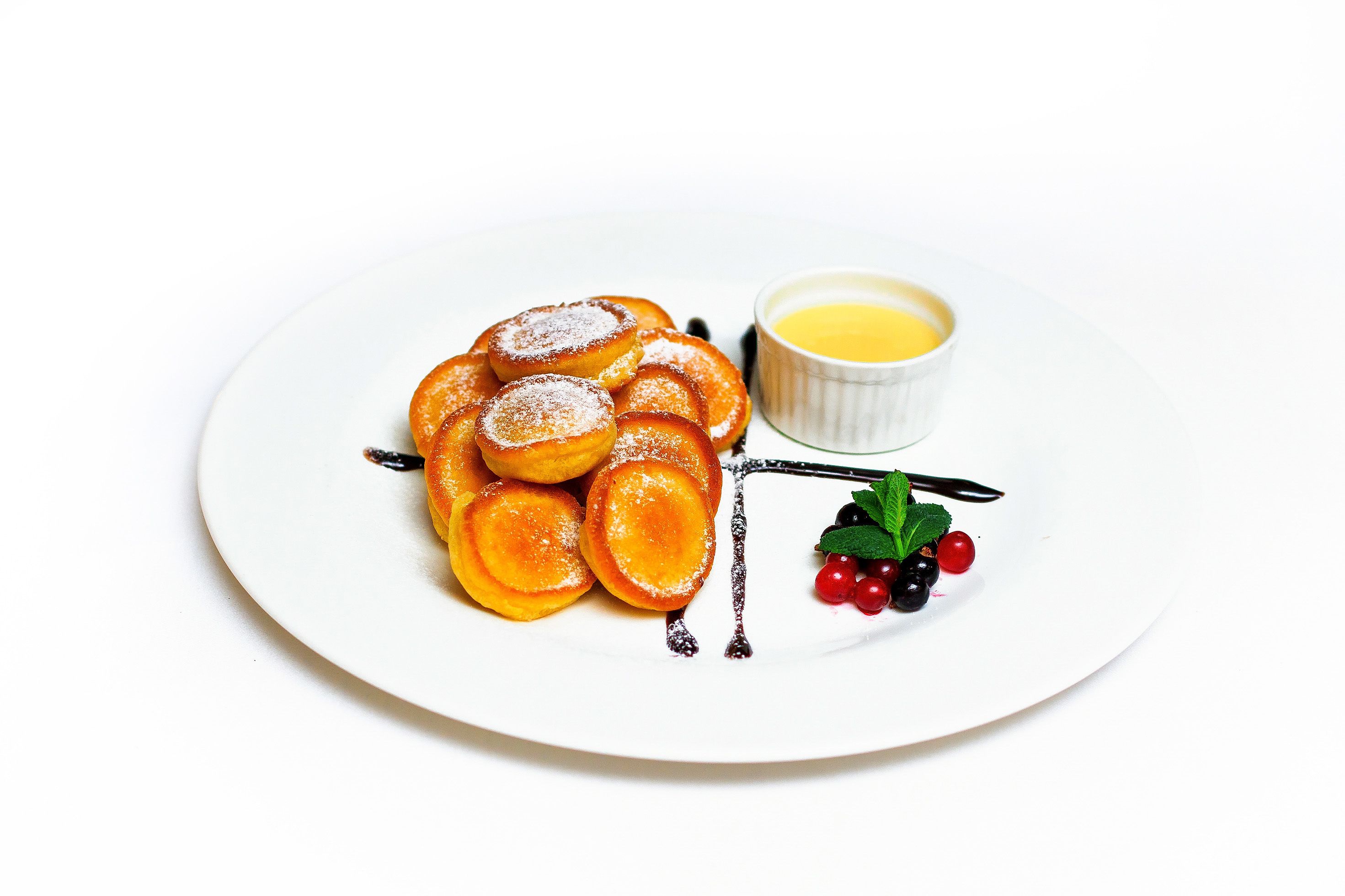 A plate with sliced pastries, a small bowl of sauce, and some berries.