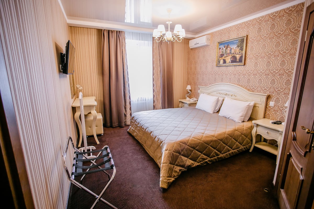 A hotel room with a bed, a chair, a nightstand, a lamp, and a painting on the wall.