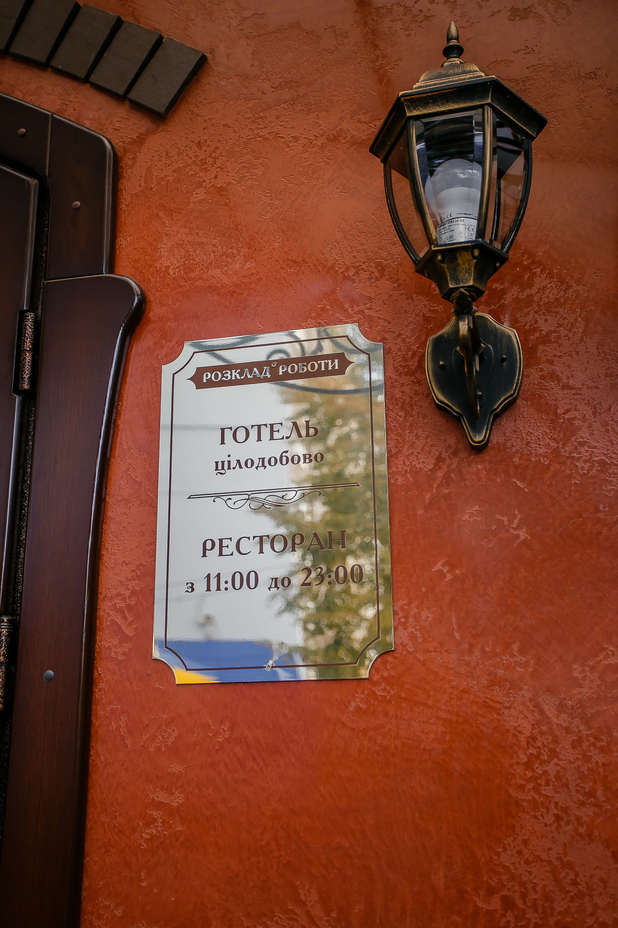 A wall-mounted sign with a restaurant operating hours and a traditional lantern.