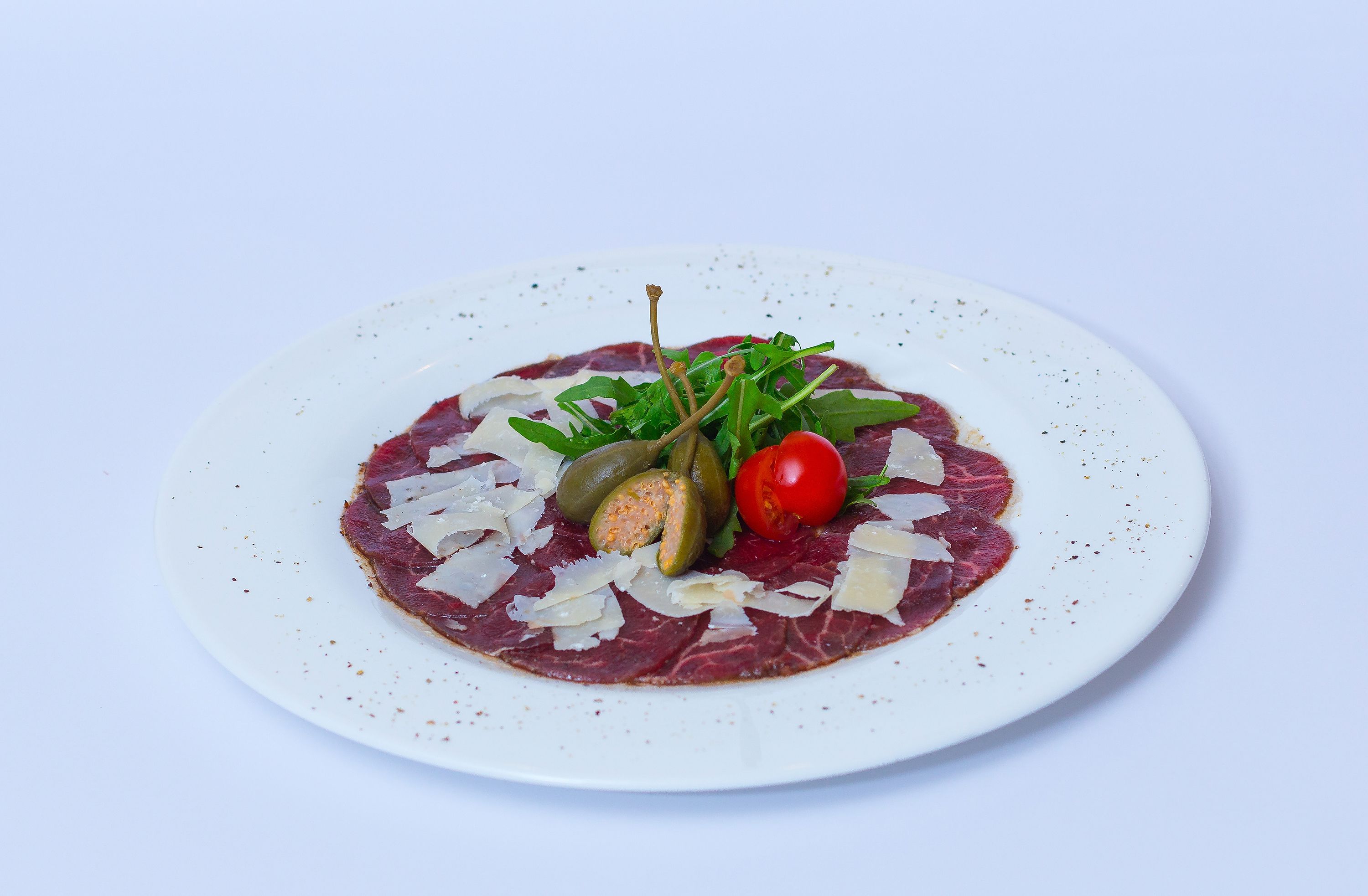 Un plato de carne cruda con verduras y queso.