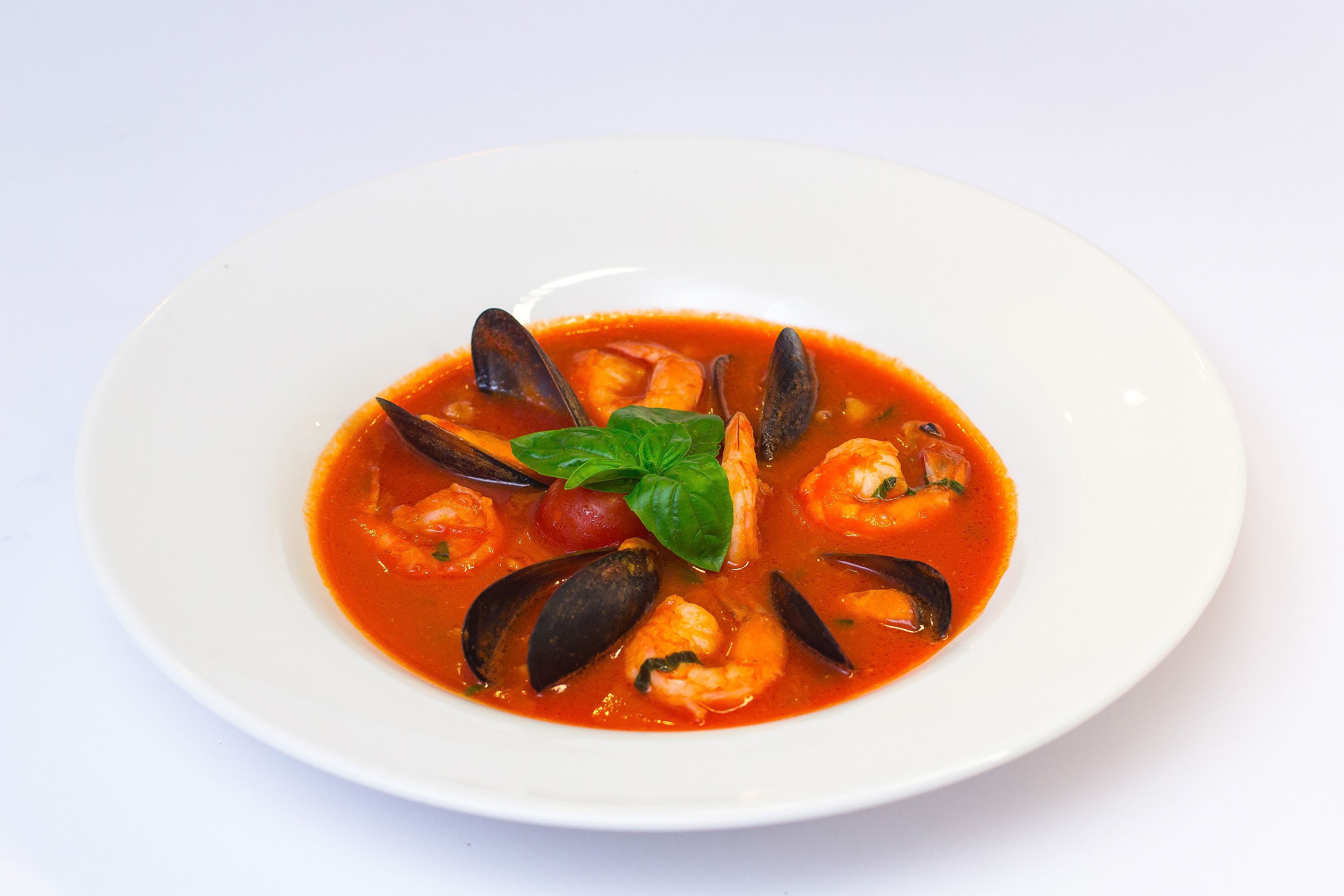 Un tazón de sopa de mariscos con mejillones y camarones, adornado con albahaca.