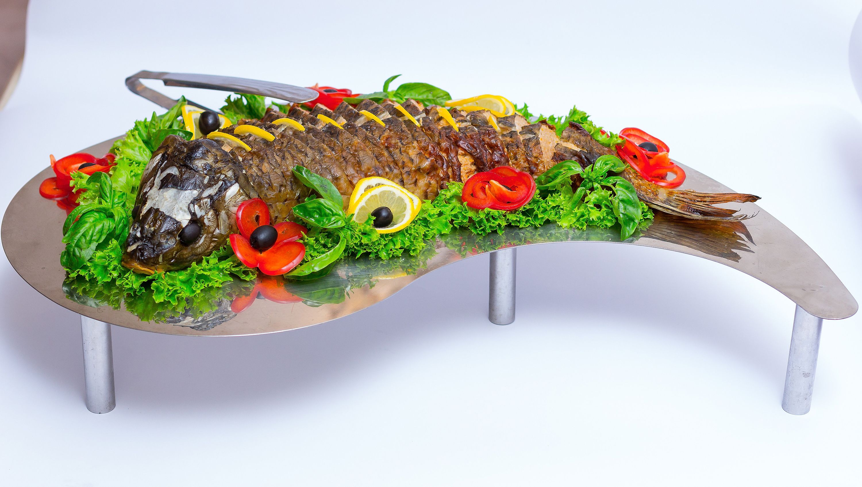 A fish carved into a decorative platter with vegetables and lemon slices.