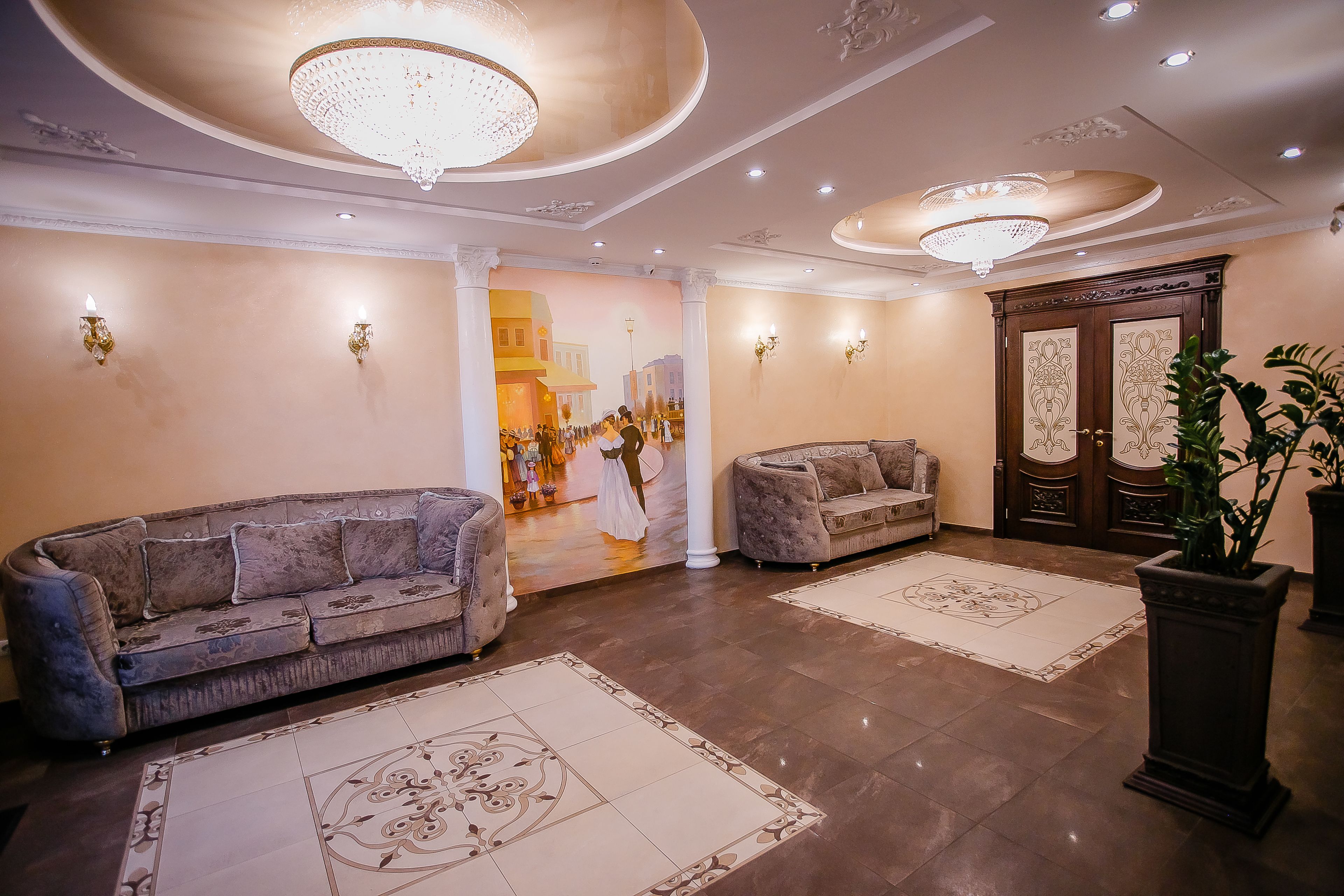 A spacious lobby with two sofas, a large chandelier, and a decorative wall mural.