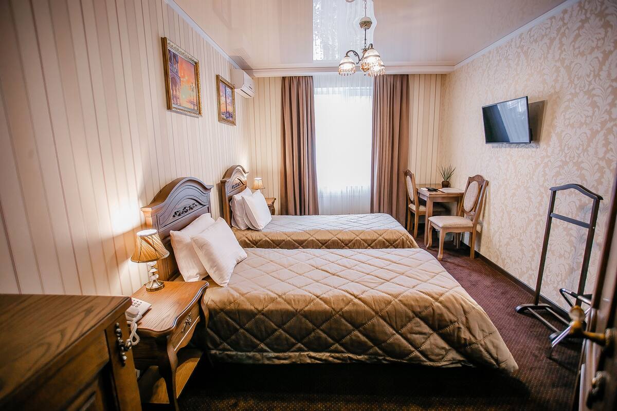 A hotel room with two beds, a desk, a chair, a TV, and a window with curtains.