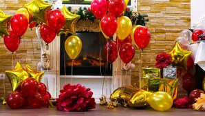 Una habitación con chimenea, rodeada de globos rojos y dorados, y un gran arreglo floral rojo.