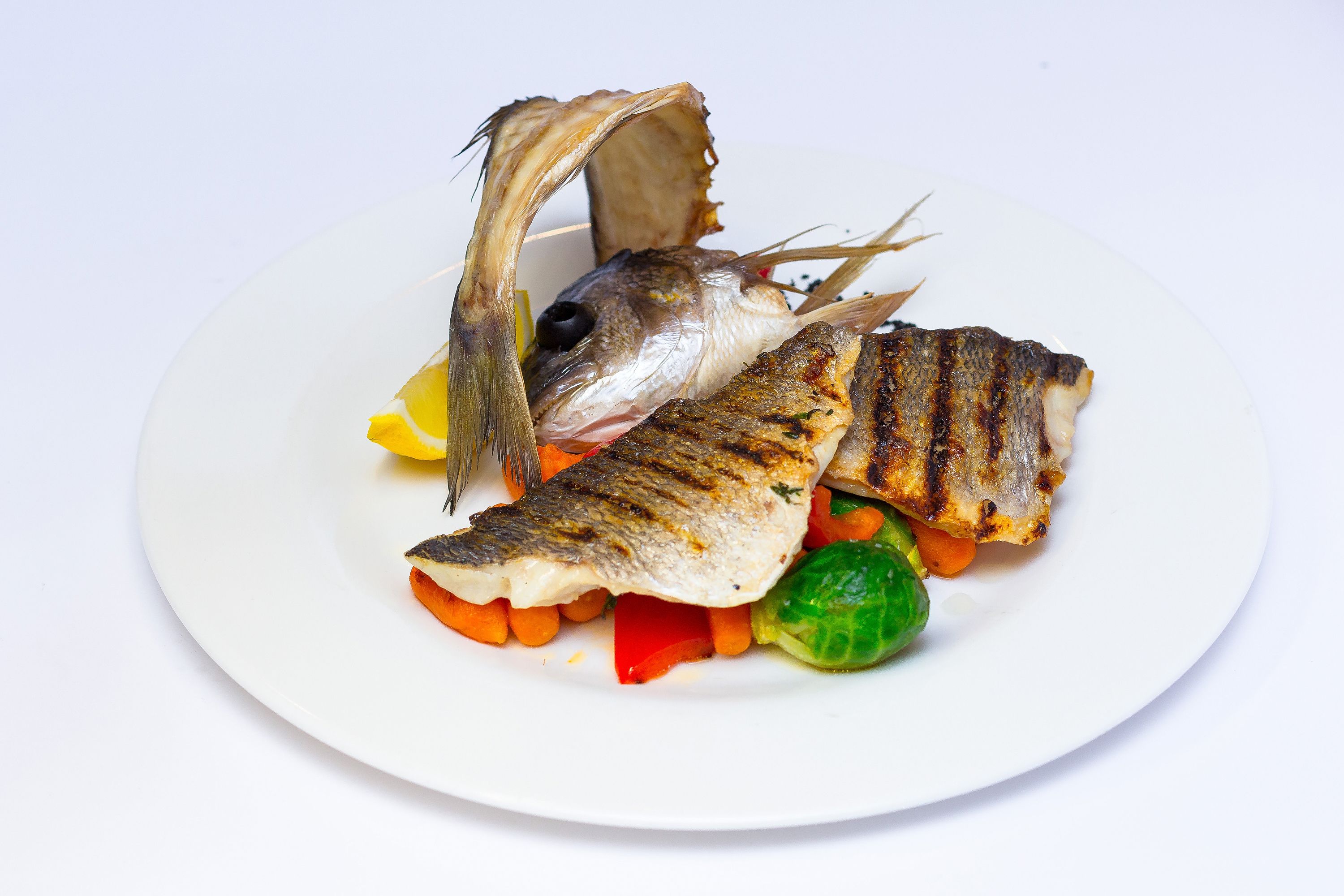 Een bord met gegrilde vis, wortelen en groente.