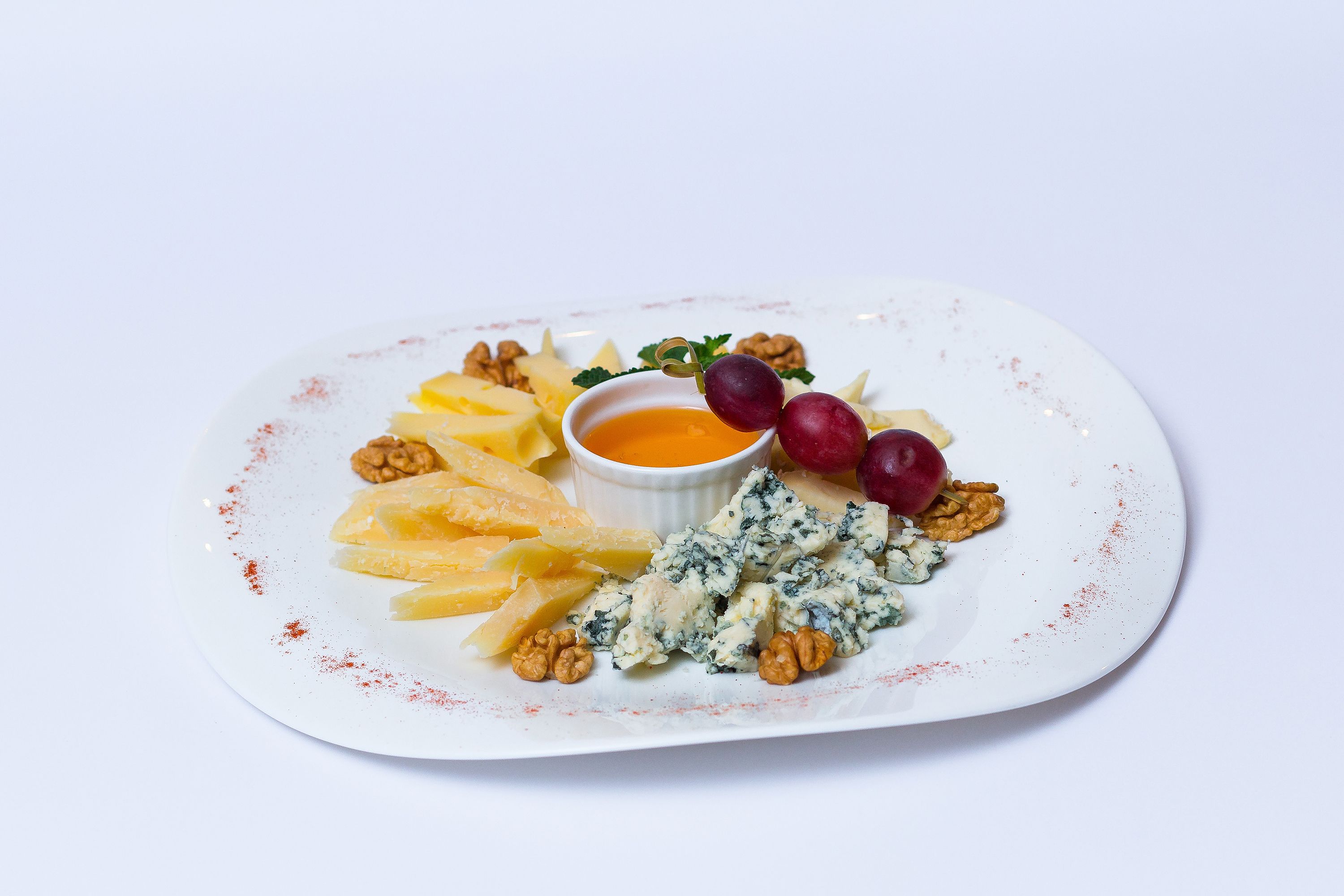 A plate with cheese, grapes, walnuts, and a small bowl of dip.