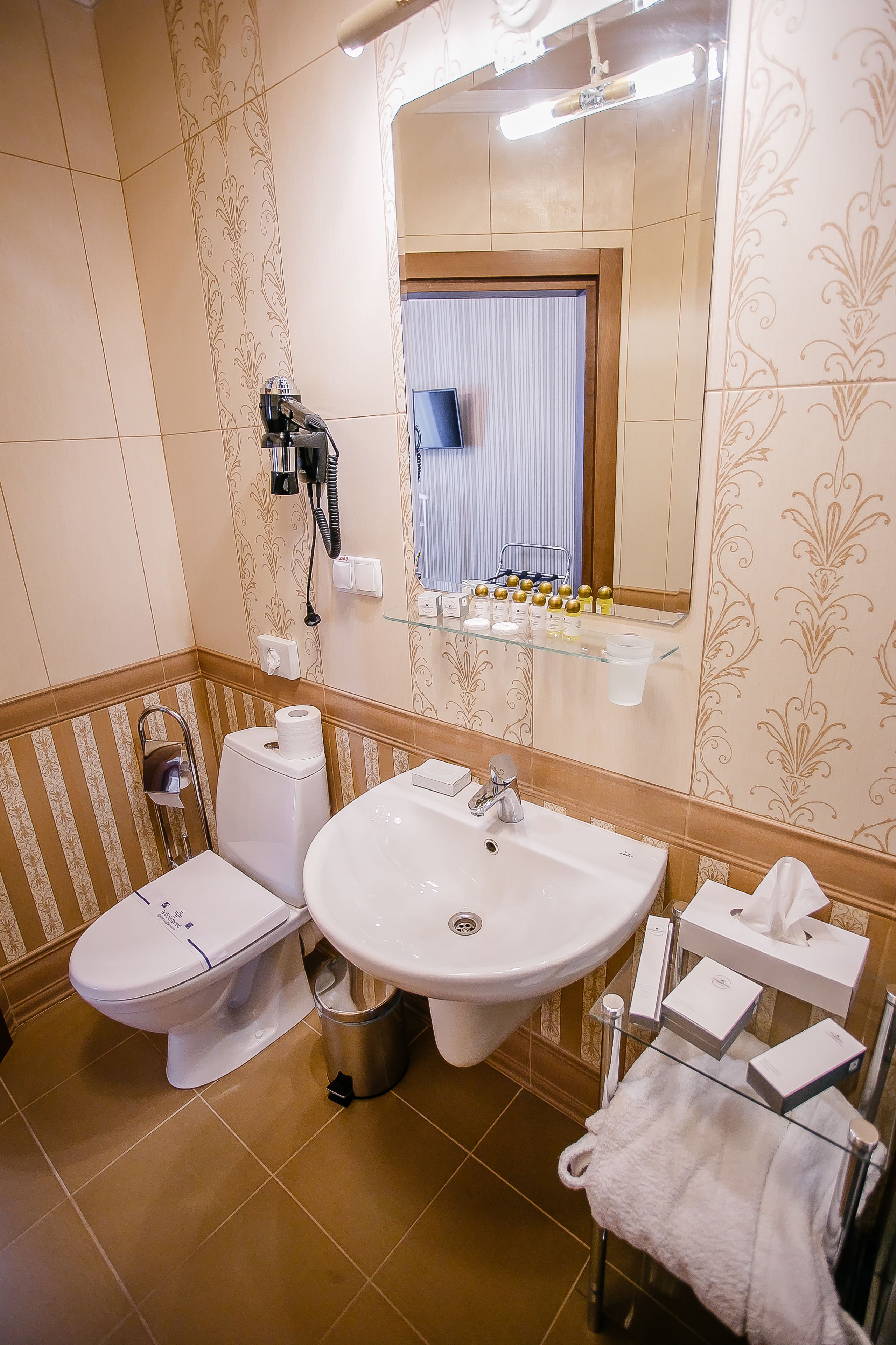 A bathroom with a toilet, bidet, sink, and a glass shelf with toiletries.