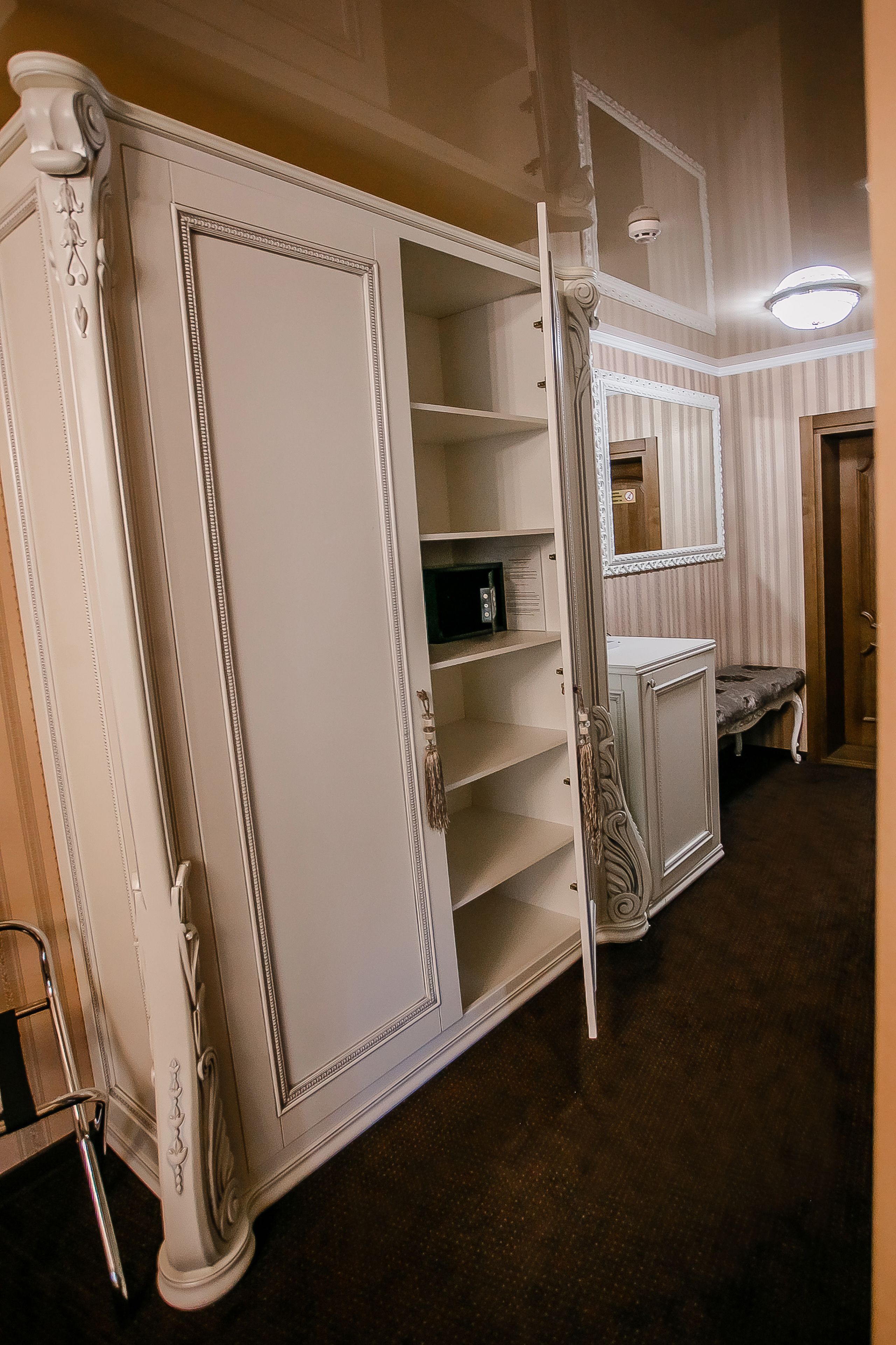 Een kamer met een grote witte garderobe, een spiegel erboven en een bankje in de hoek.