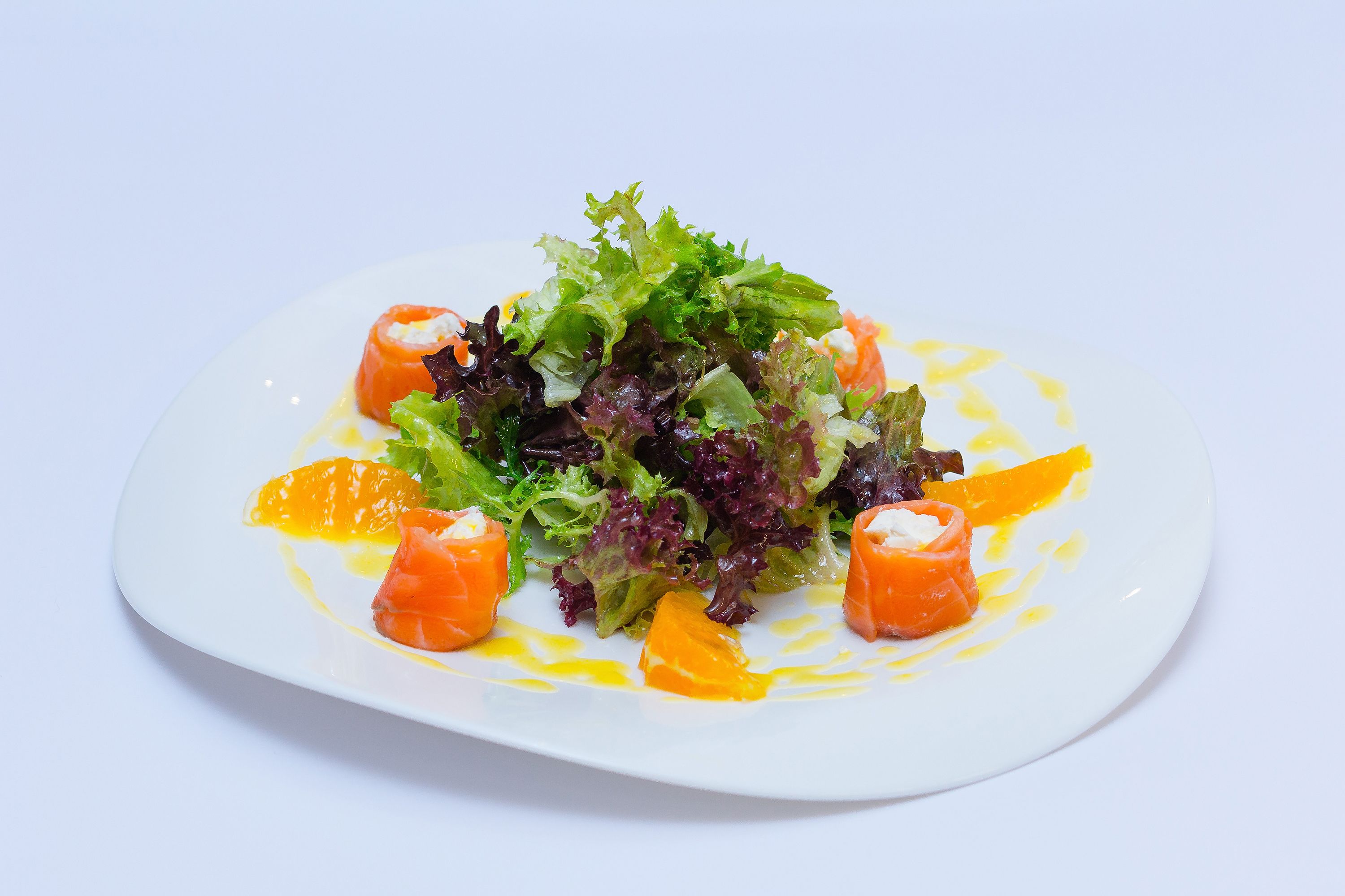 Une assiette blanche contenant une salade composée de feuilles vertes et de segments d’orange, le tout arrosé d’une vinaigrette.