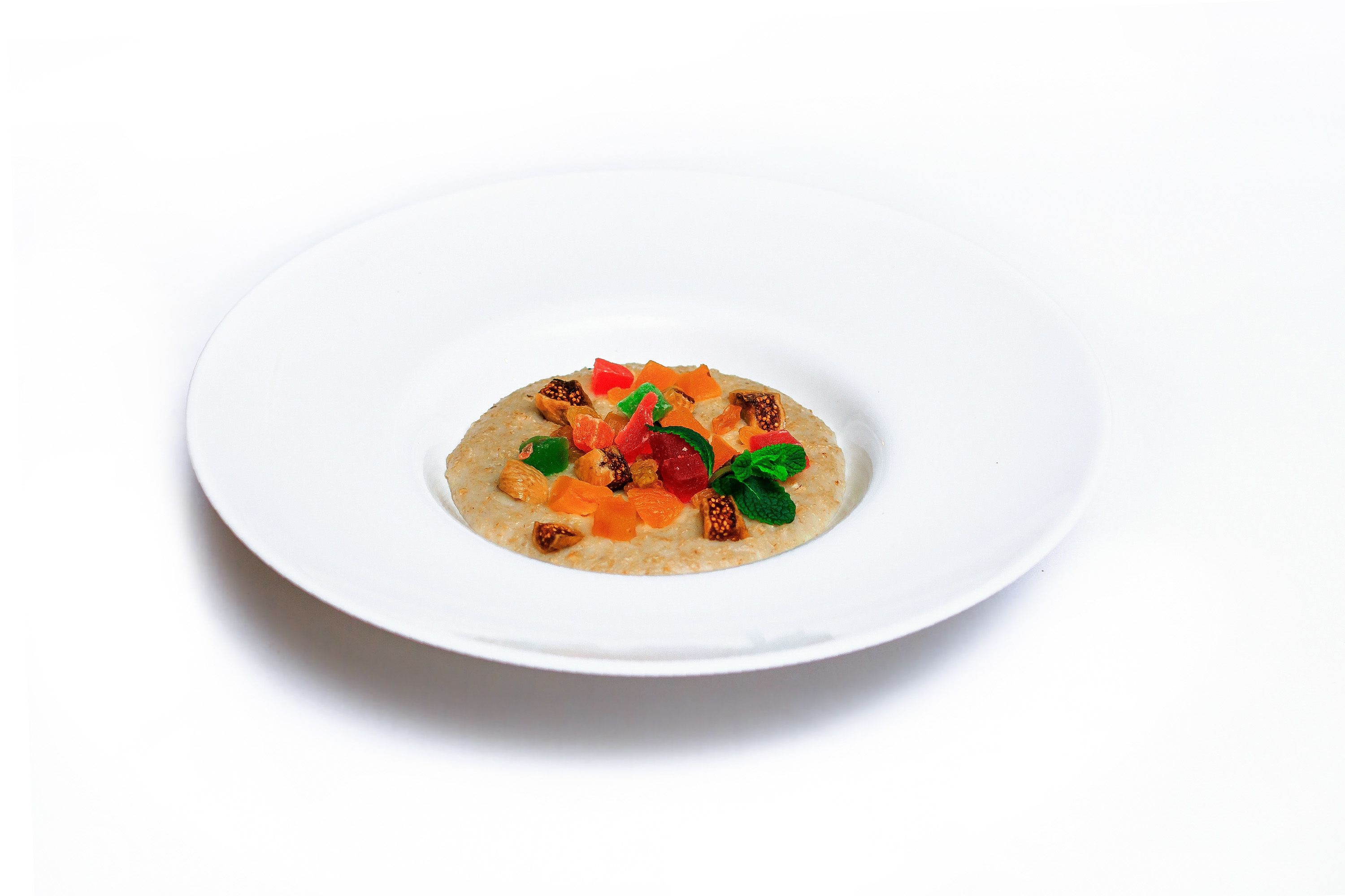 A white plate with a dessert consisting of a base layer, topped with various fruits and nuts.