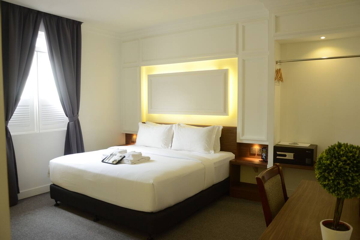 A hotel room with a large bed, bedside tables, a desk, and a potted plant.