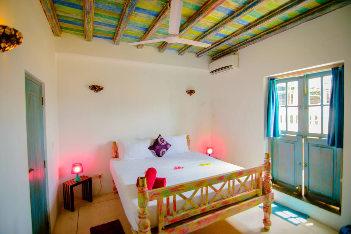 A bedroom with a bed, a nightstand, a window with curtains, and a ceiling fan.